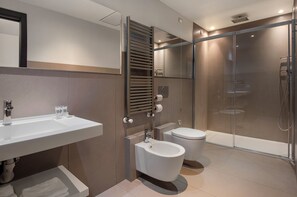 A modern bathroom with a white sink, two toilets, a glass-enclosed shower, and a towel rack.