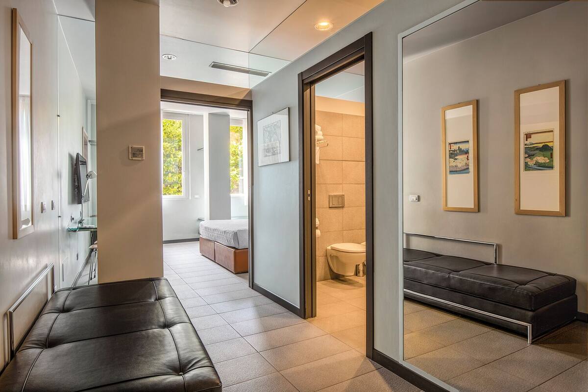 A modern hotel room with a large bed, a seating area, a bathroom, and artwork on the walls.