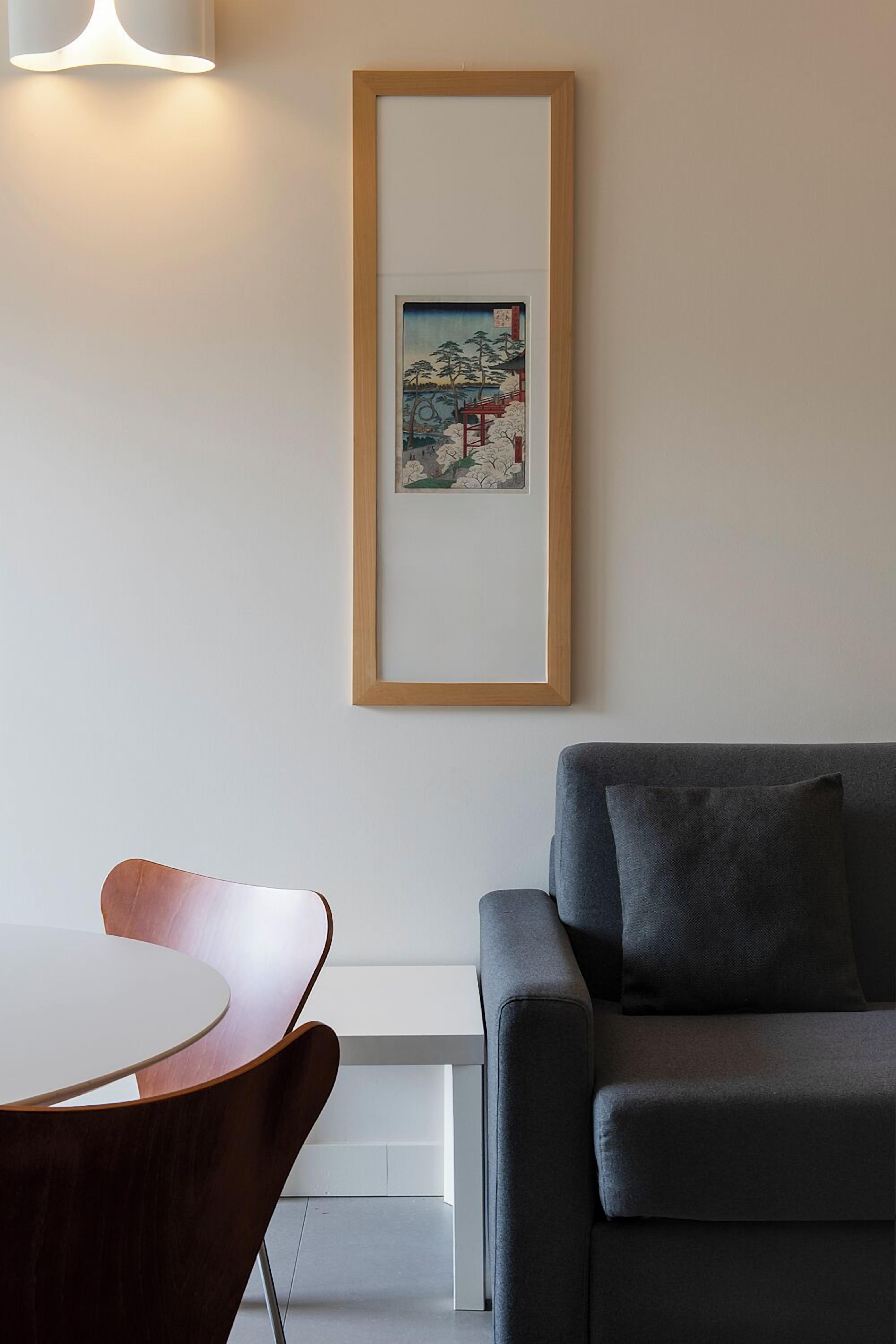 Una sala de estar moderna con un sofá gris, una silla de madera y una obra de arte enmarcada en la pared.