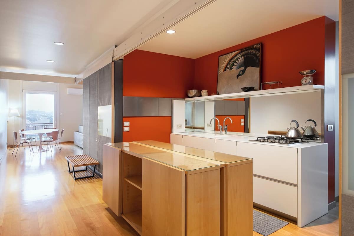 A modern kitchen with a central island, a dining area with a table and chairs, and a view of the city through large windows.