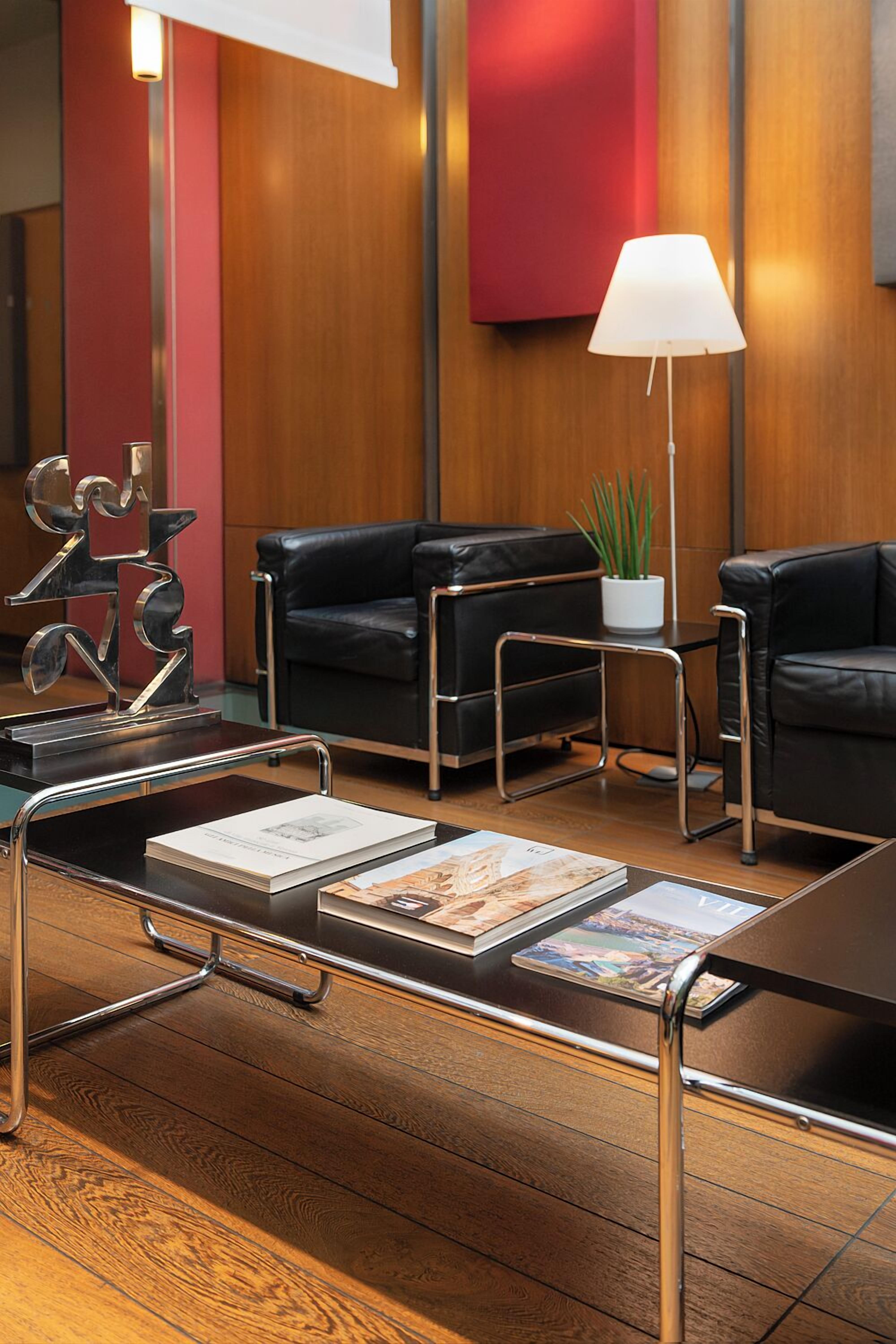 A modern lobby with leather sofas, a glass coffee table, and a minimalist decor including a lamp and a plant.