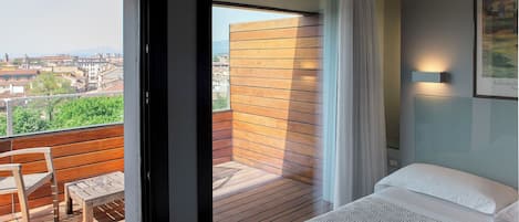 Habitación de hotel con balcón, cama, una silla y vistas a la ciudad.
