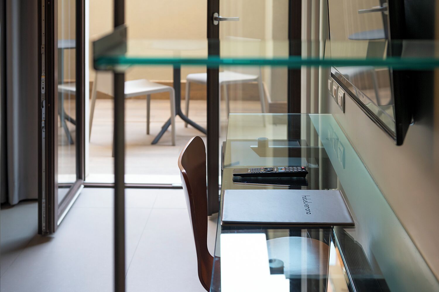 A modern office space with a glass partition, a desk with a laptop, and a chair.