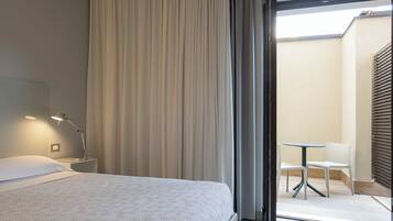 Ein Hotelzimmer mit Bett, Nachttischlampe und Blick auf einen Außenbereich mit Sitzgelegenheiten.
