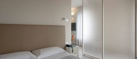 A modern hotel room with a large bed, a bedside table, a desk, and a sliding door leading to a bathroom.