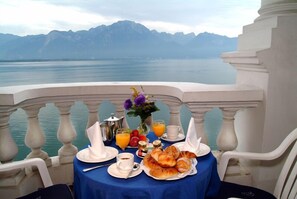 A table set with breakfast items, including croissants, fruit, and juice, overlooking a lake with mountains in the background. - Hôtel du Grand Lac Excelsior (Montreux)