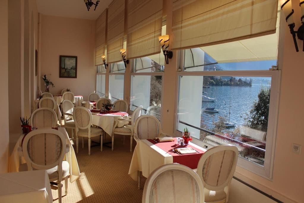 Un área de comedor con mesas y sillas, ventanas amplias con vistas a un cuerpo de agua y un cuadro en la pared.