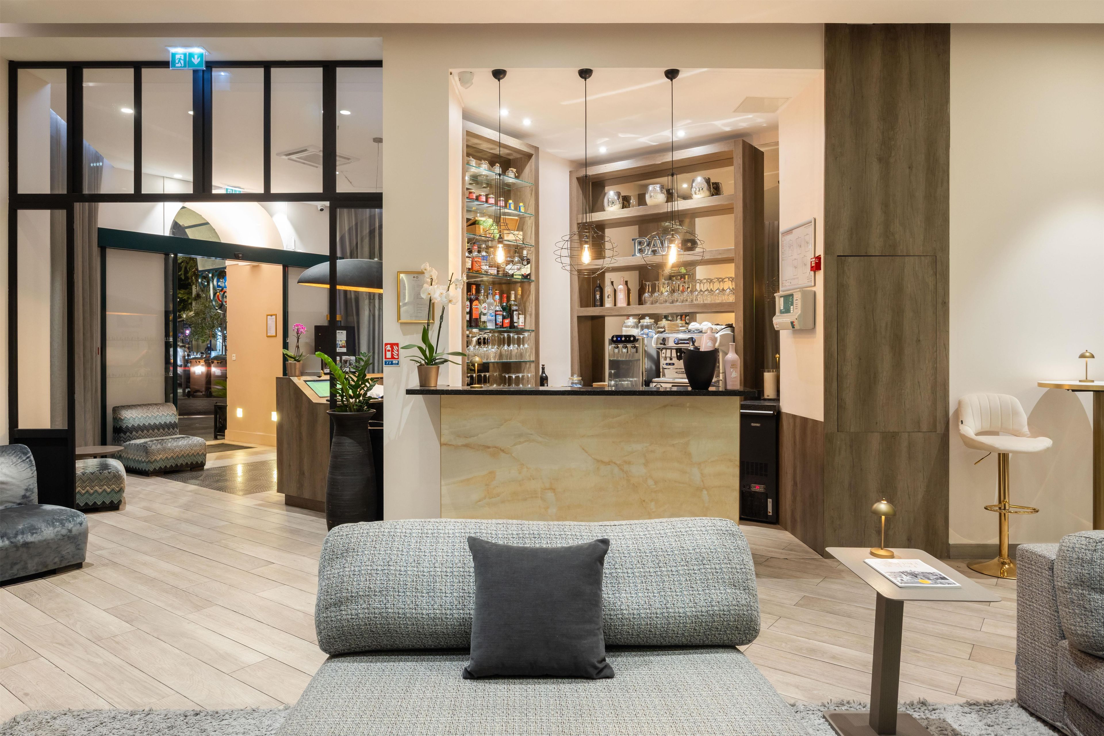 Un moderno vestíbulo de hotel con una recepción, zona de estar y un bar-lounge con estantes llenos de botellas y vasos.