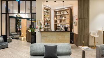 Un moderno vestíbulo de hotel con una recepción, zona de estar y un bar-lounge con estantes llenos de botellas y vasos.