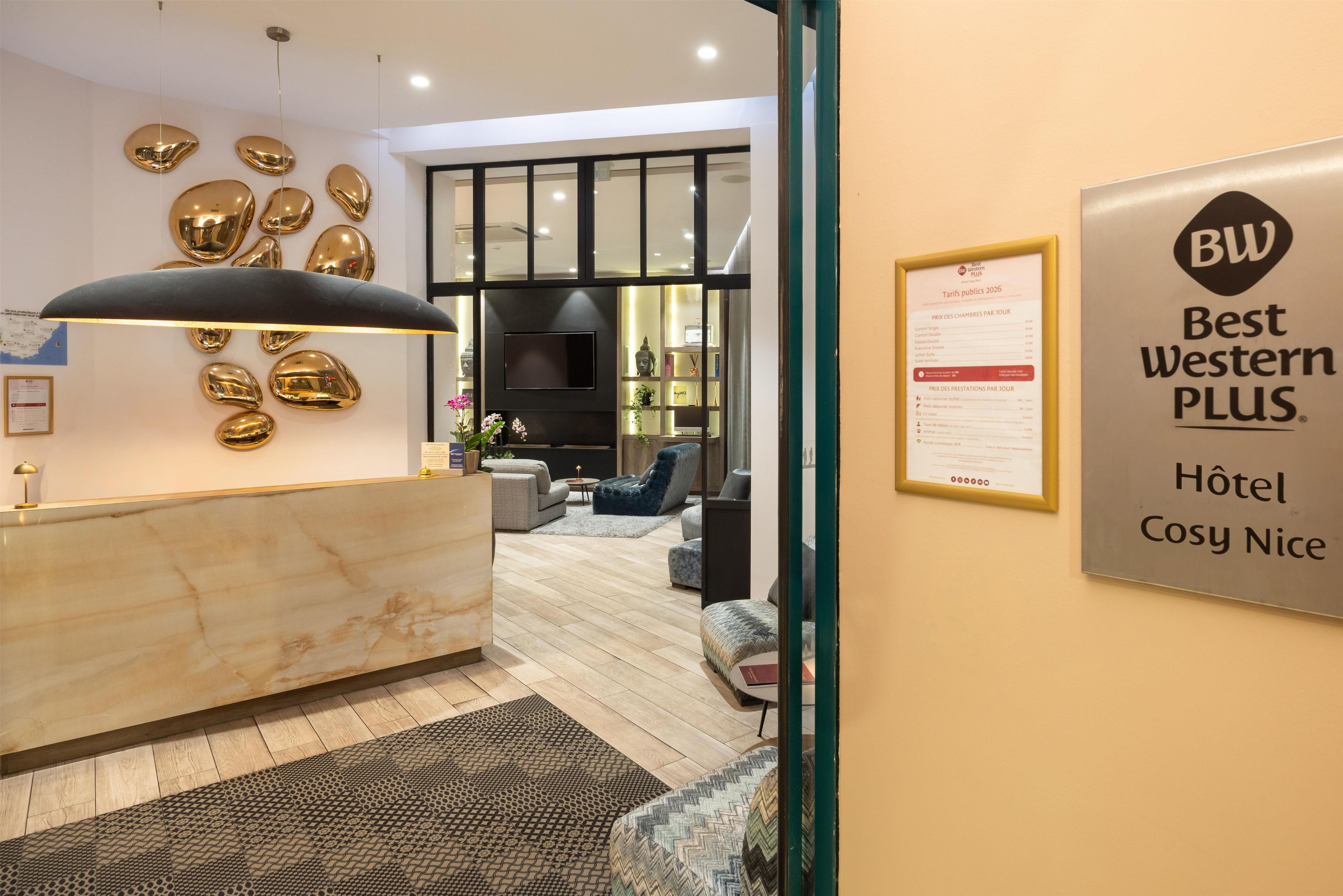 A hotel reception area with a marble counter, a modern chandelier, and a wall-mounted television.