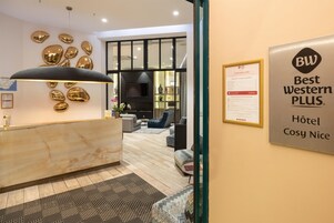 Et hotellets receptionsområde med en marmordisk, en moderne lysekrone og et tv ophængt på væggen.