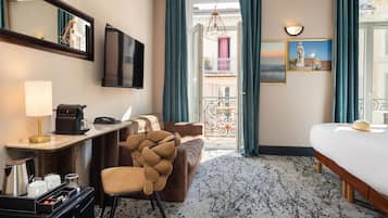 Een hotelkamer met een bed, een bureau met telefoon, een stoel, een koffiezetapparaat en uitzicht op zee vanaf een balkon.