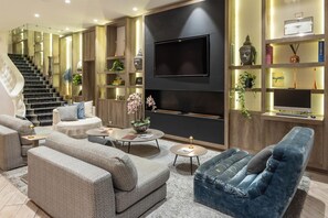 A modern living room with a staircase, sofas, a coffee table, and a TV wall unit.