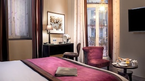 A hotel room with a bed, a desk with a lamp, a chair, a dining table with breakfast items, and a window with a view of buildings. - Best Western Plus Nice Cosy Hôtel (Nice)