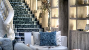 A staircase with patterned steps, a white cushioned seating area with pillows, and a wooden bookshelf with decorative items. - Best Western Plus Nice Cosy Hôtel (Nice)