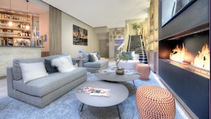 A modern living room with a sofa, coffee table, and ottoman, a fireplace, and a bar area with shelves of bottles and glasses. - Best Western Plus Nice Cosy Hôtel (Nice)