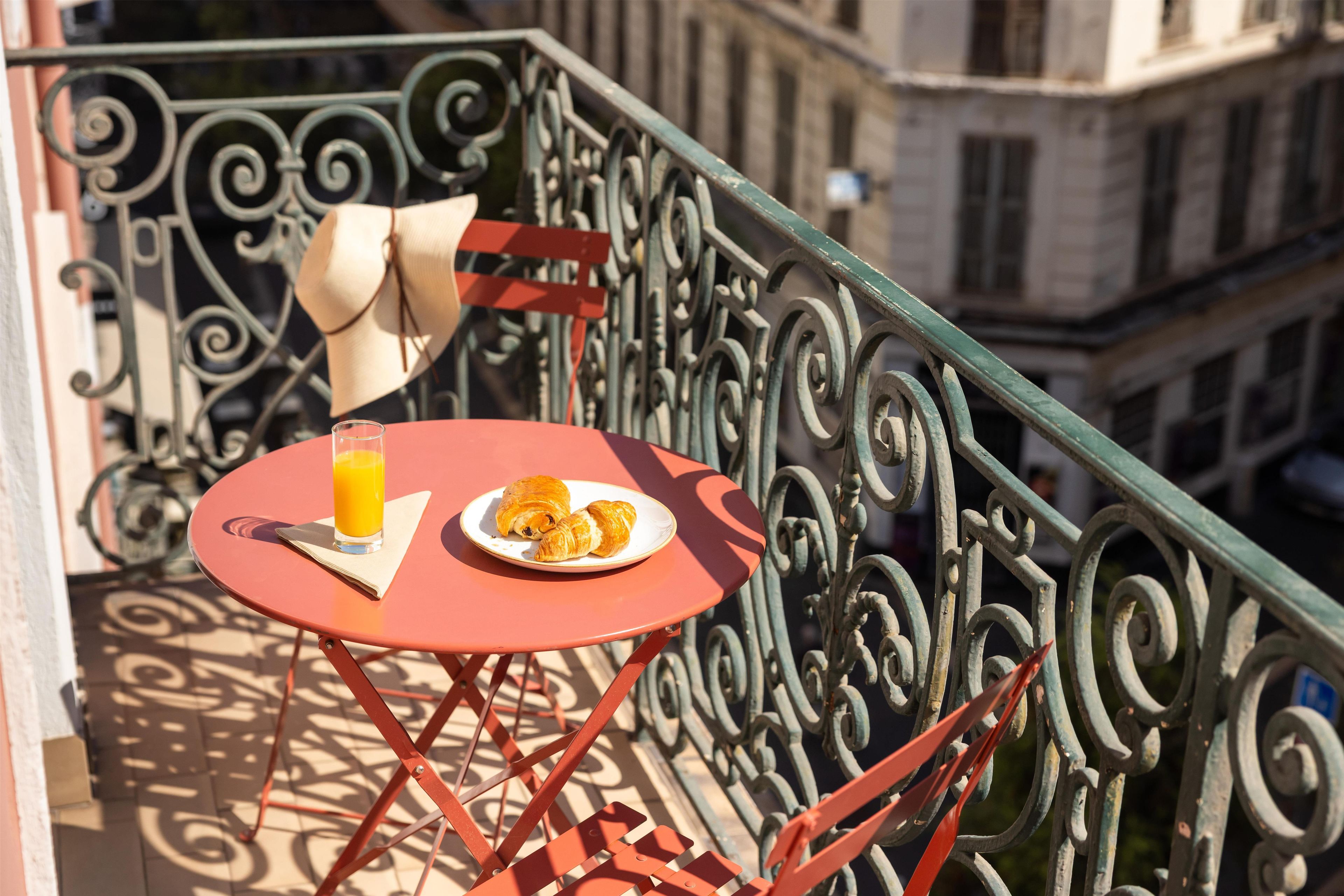 Una pequeña mesa al aire libre con un vaso de jugo de naranja y croissants sobre un mantel rojo.