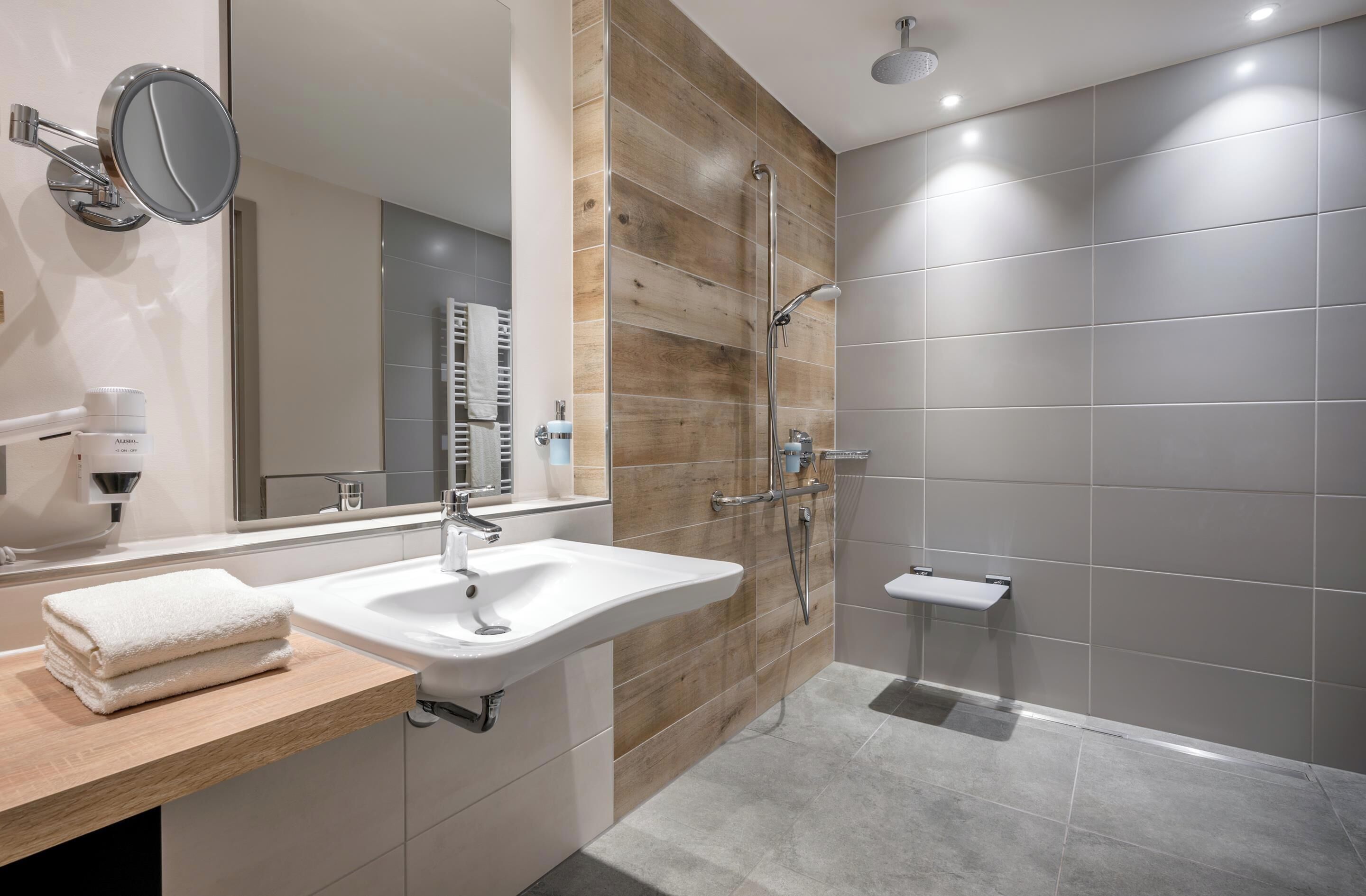 A modern bathroom with a wooden accent wall, a large mirror, a sink, and a shower area.