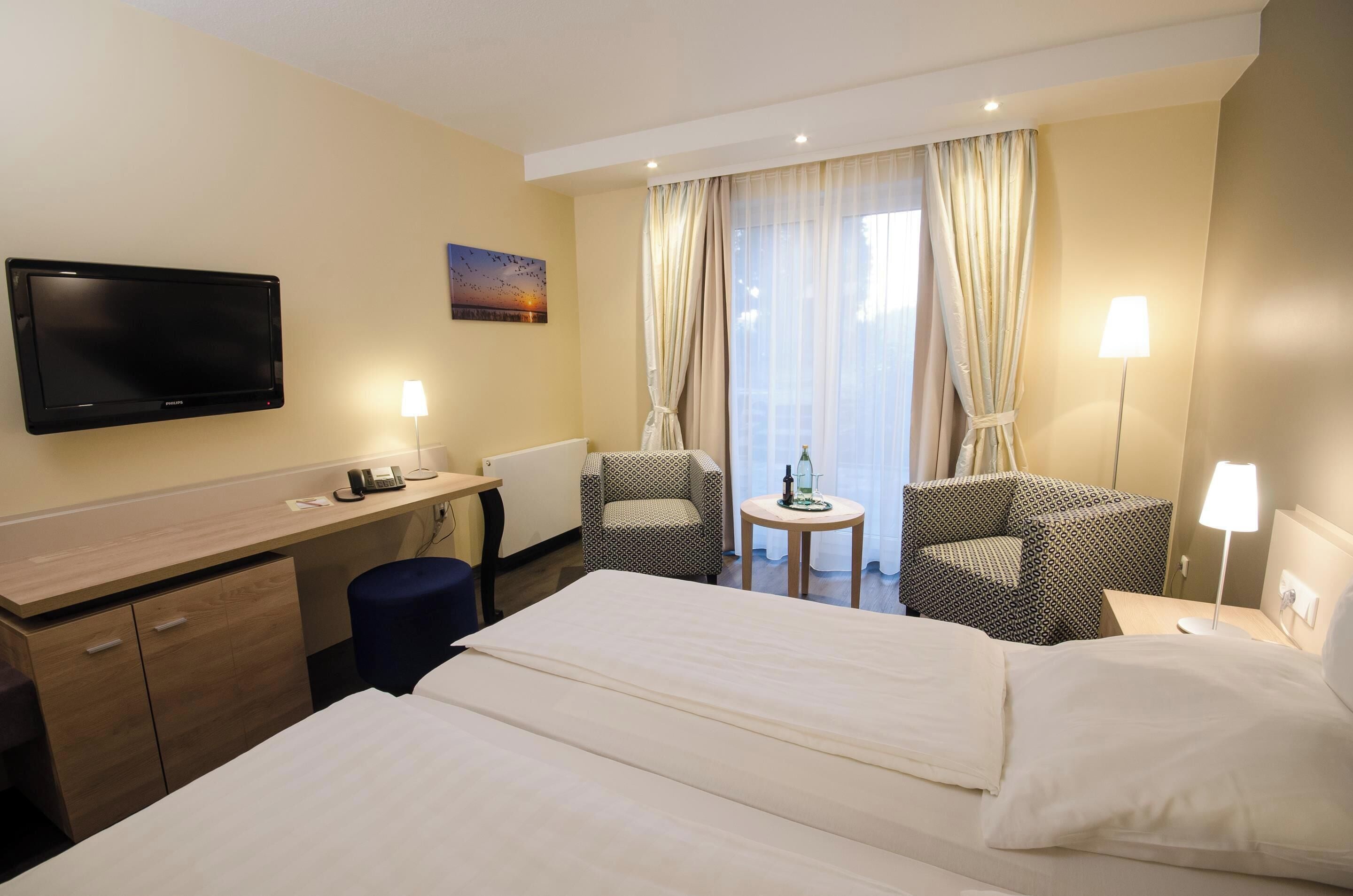 Ein Hotelzimmer mit Bett, Schreibtisch, Stuhl, Fernseher und einem Fenster mit Vorhängen.