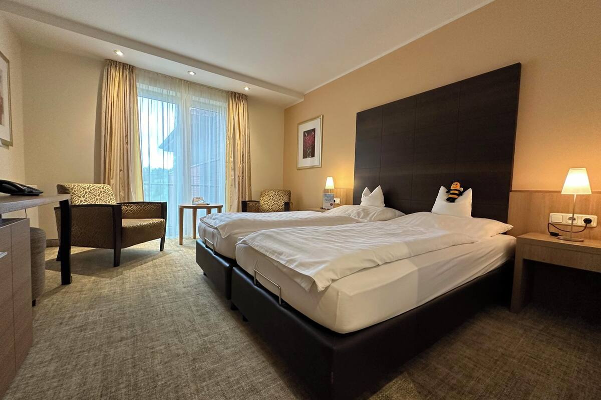 Hotellihuone, jossa on kaksi sänkyä, työpöytä, tuoli ja pieni pöytä.