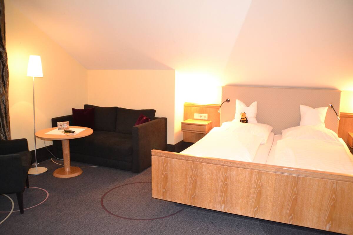 Hotellihuone, jossa on sänky, pieni pyöreä pöytä, sohva ja yöpöytä.