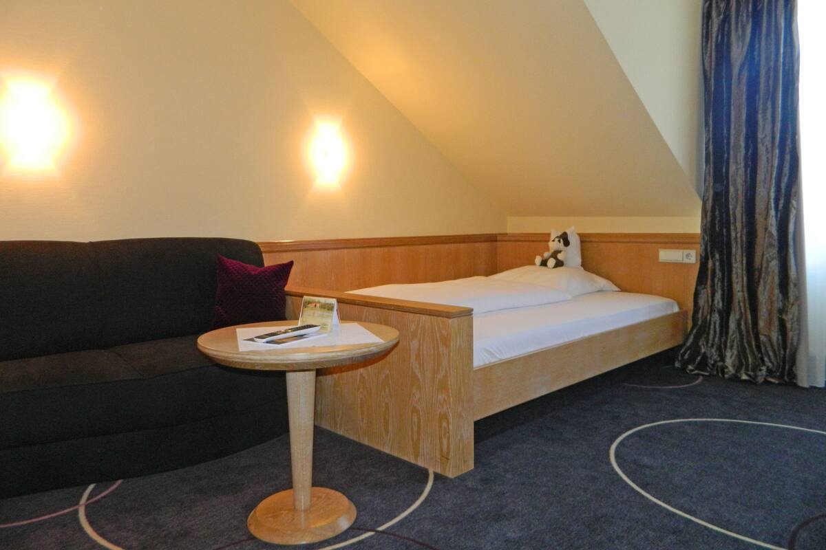 Hotellihuone, jossa on sänky, pieni pyöreä pöytä, jossa on kaukosäädin, tyyny ja sohva.
