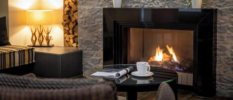Una habitación acogedora con chimenea, una mesa con una taza y un libro, y dos plantas en macetas sobre una pared de piedra.