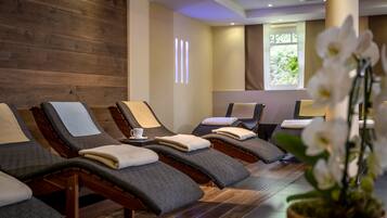 Um espaço de spa com paredes de madeira, várias cadeiras de massagem, uma orquídea em vaso e uma janela com vista para o verde.