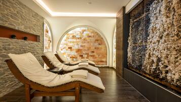 A spa area with three sun loungers, a stone wall, and a textured wall art piece.