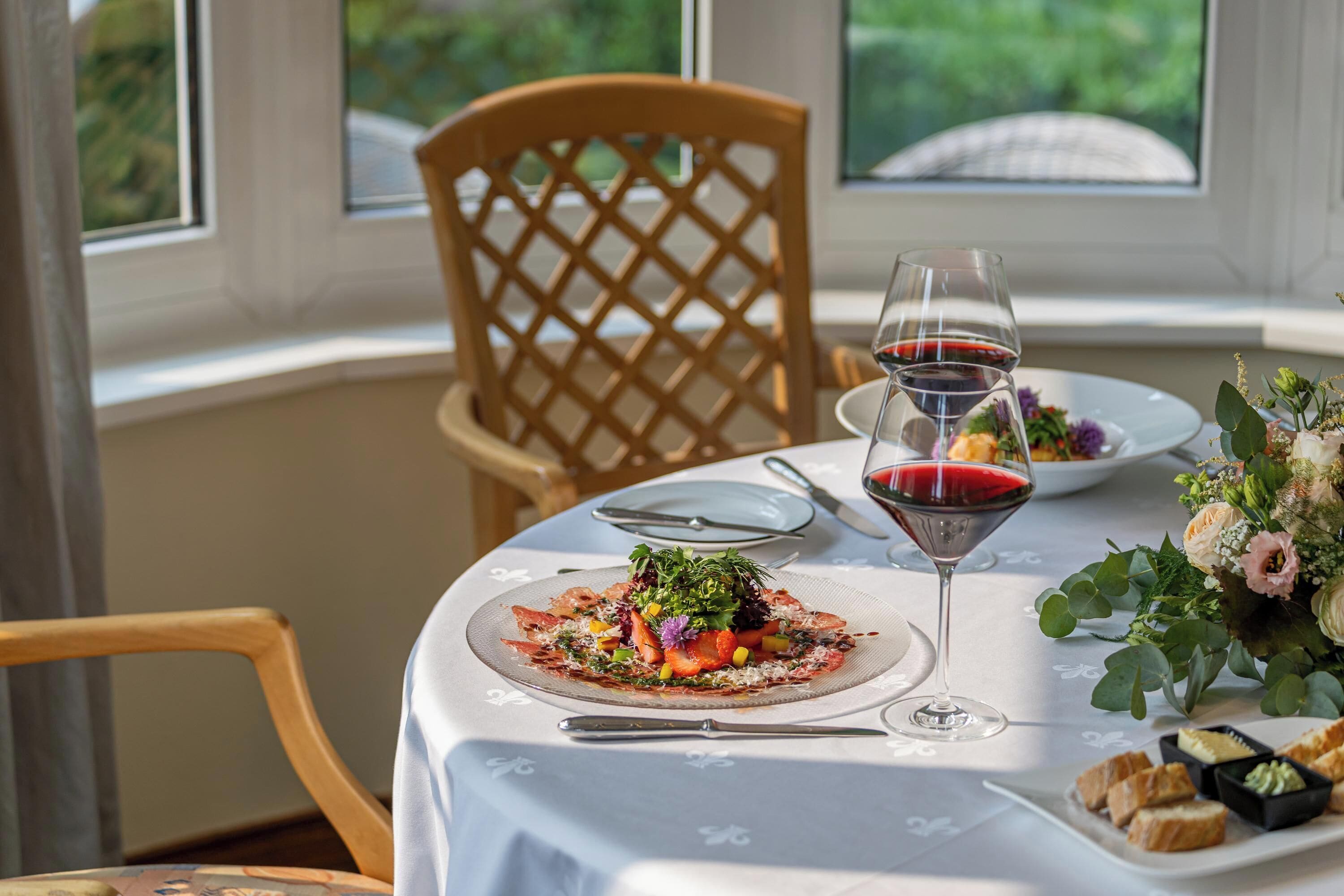 A dining table set with plates, cutlery, and a glass of red wine.
