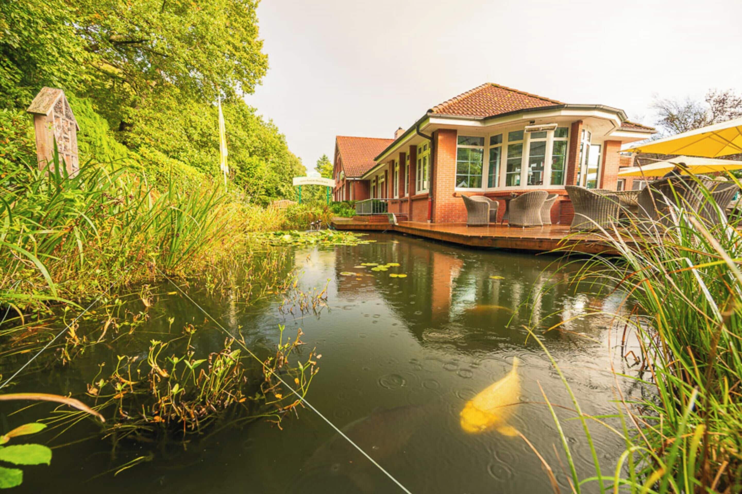 Un bâtiment situé au bord d’un canal, doté d’un patio couvert, entouré d’une végétation luxuriante et bordé d’une étendue d’eau paisible.