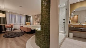 A modern hotel room with a bed, a sitting area with a chair and a table, a bathroom with a bathtub and a shower, and a large mirror.
