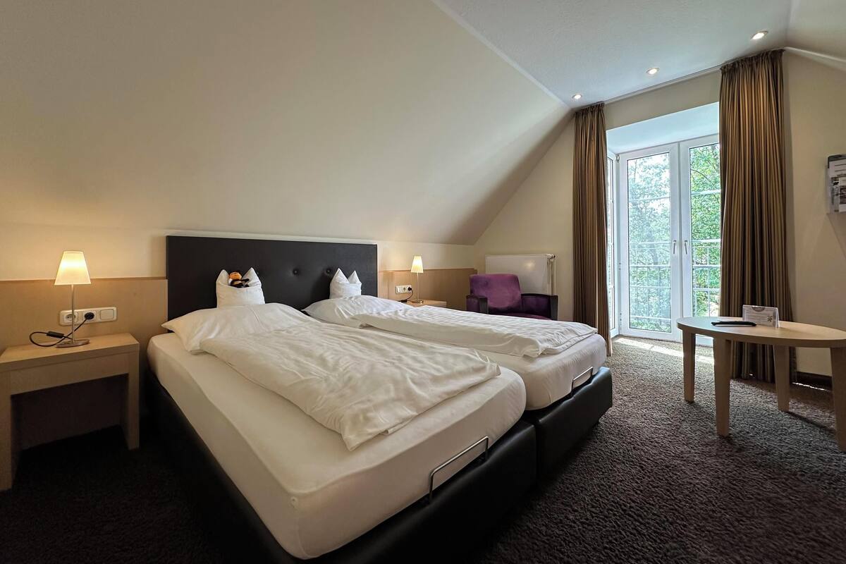 Hotellihuone, jossa on kaksi sänkyä, pieni pöytä, tuoli ja näkymä ulos.