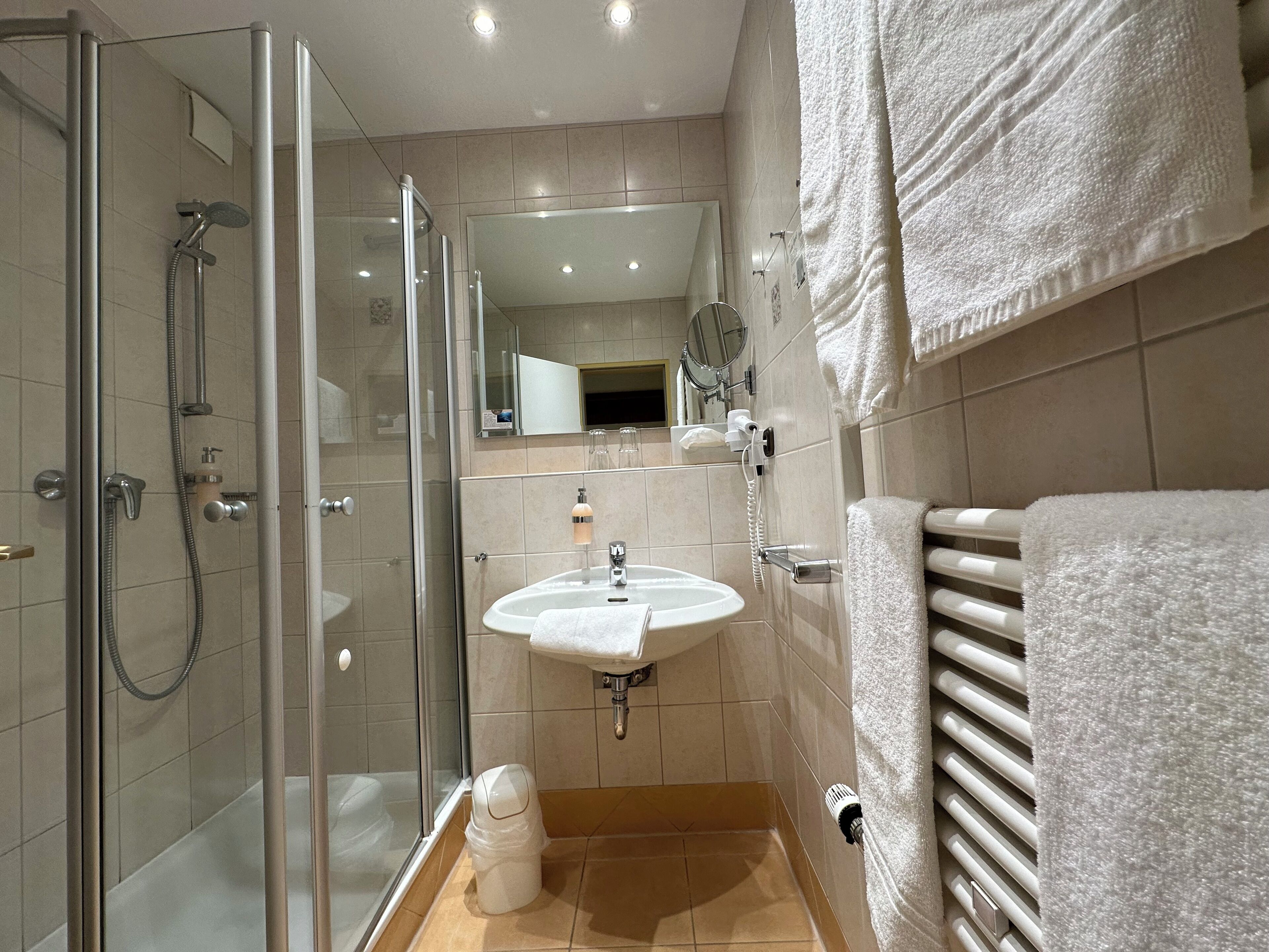 Un baño moderno con ducha de vidrio, lavamanos con toallero y espejo sobre el lavamanos.