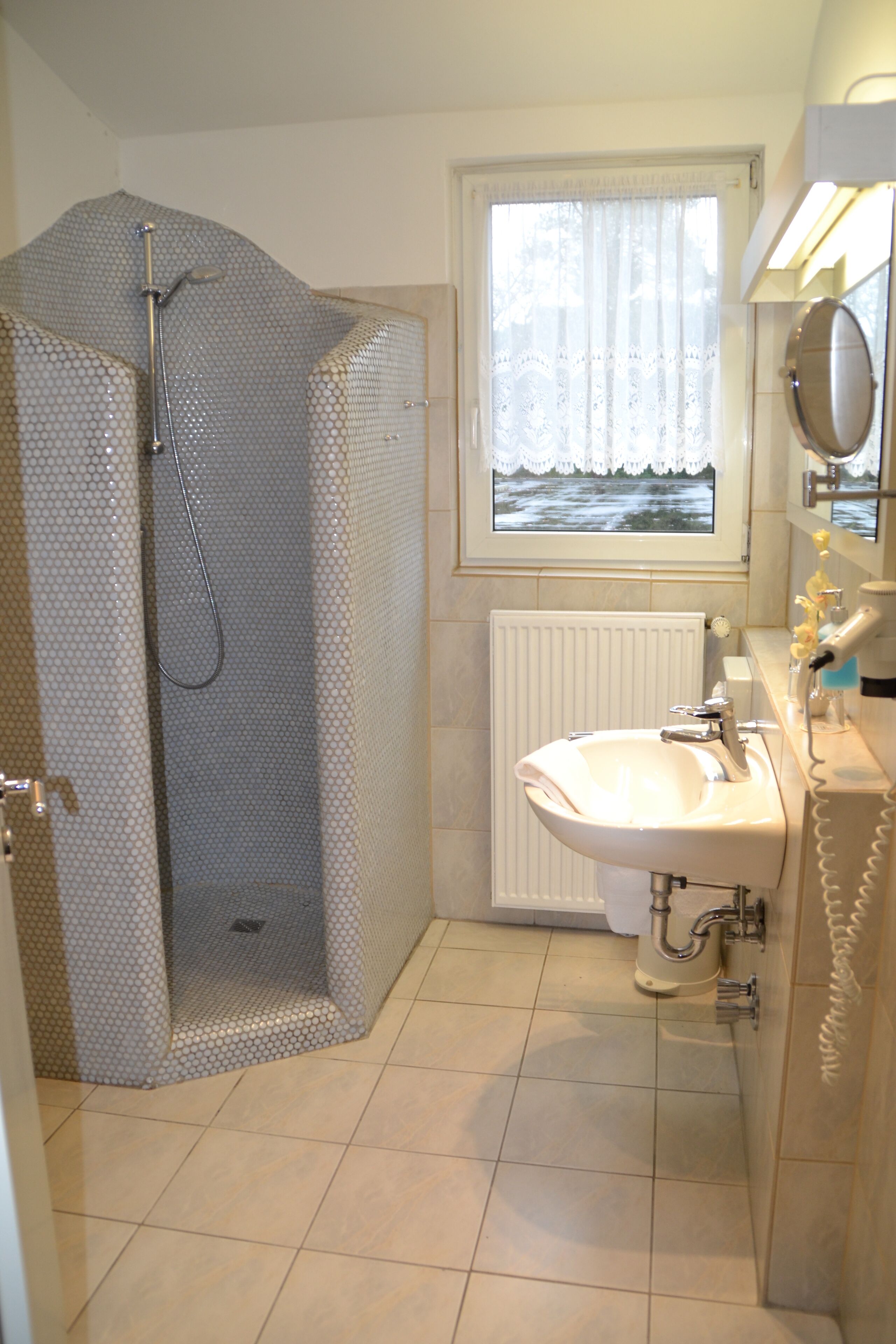 Ein Badezimmer mit Dusche, Waschbecken, Fenster mit Meerblick und Heizkörper.