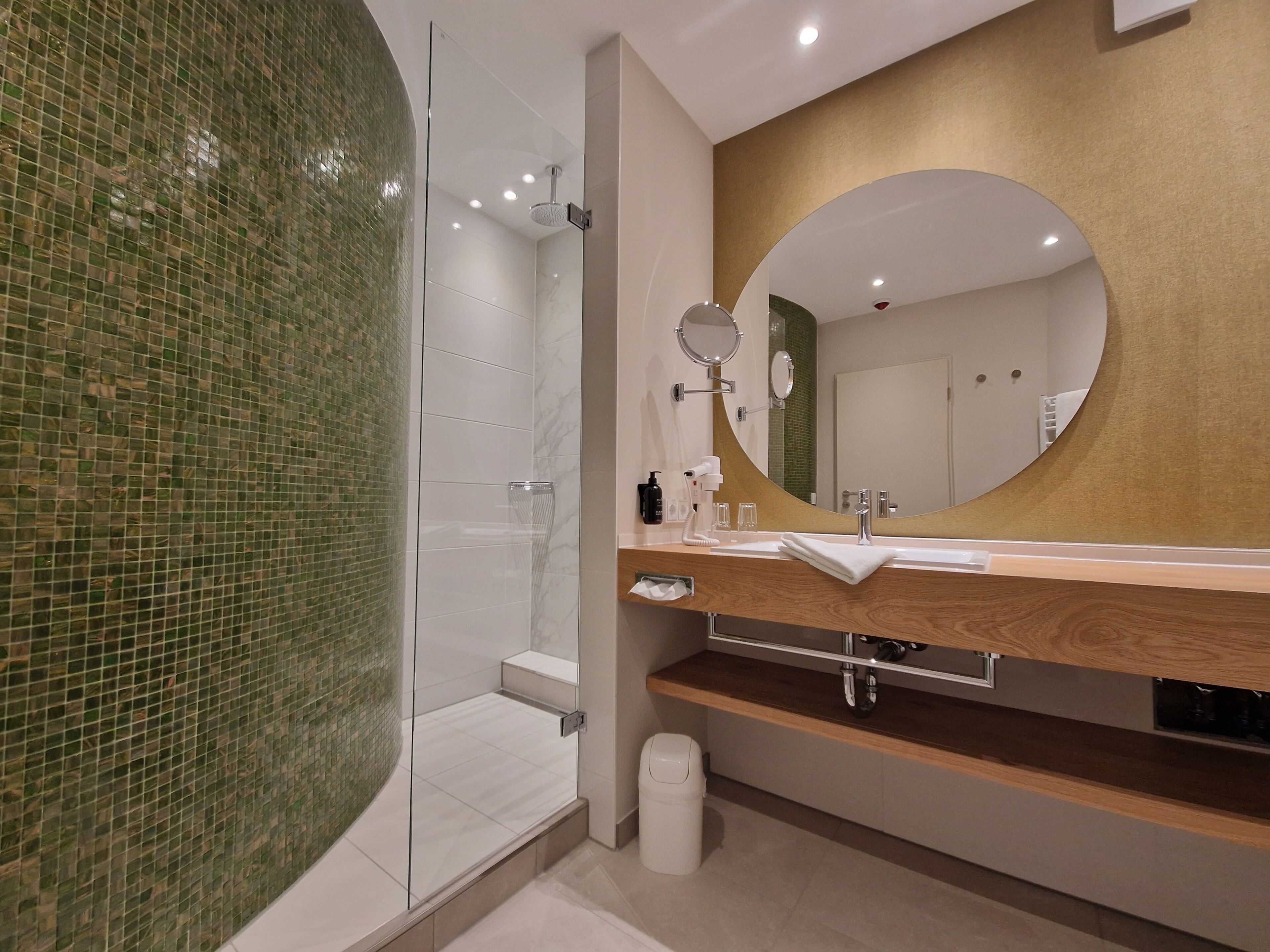 A modern bathroom with a glass shower enclosure, a wooden vanity, a large mirror, and a tiled wall.