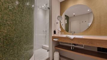 A modern bathroom with a glass shower enclosure, a wooden vanity, a large mirror, and a tiled wall.
