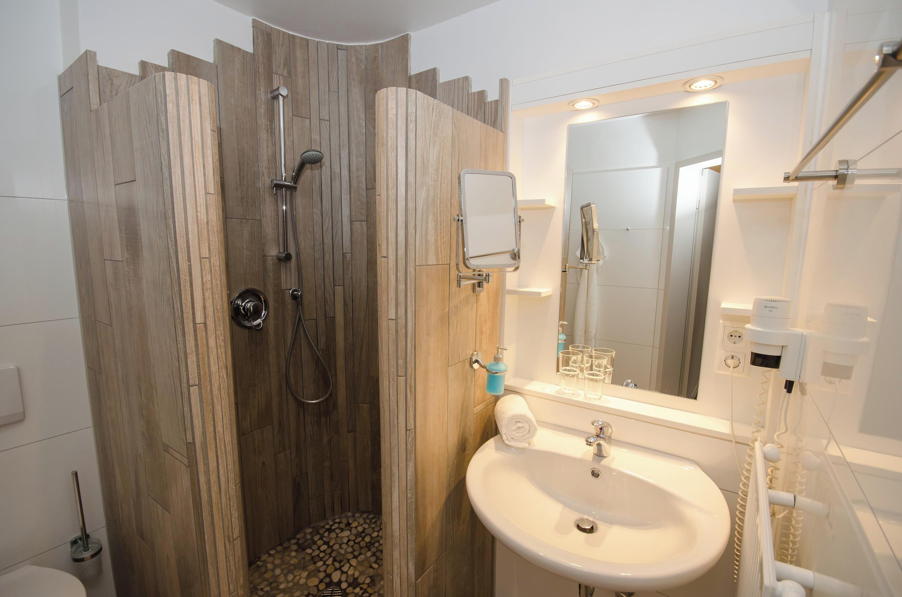 Un baño moderno con cabina de ducha de madera, un lavabo blanco y un espejo sobre él.