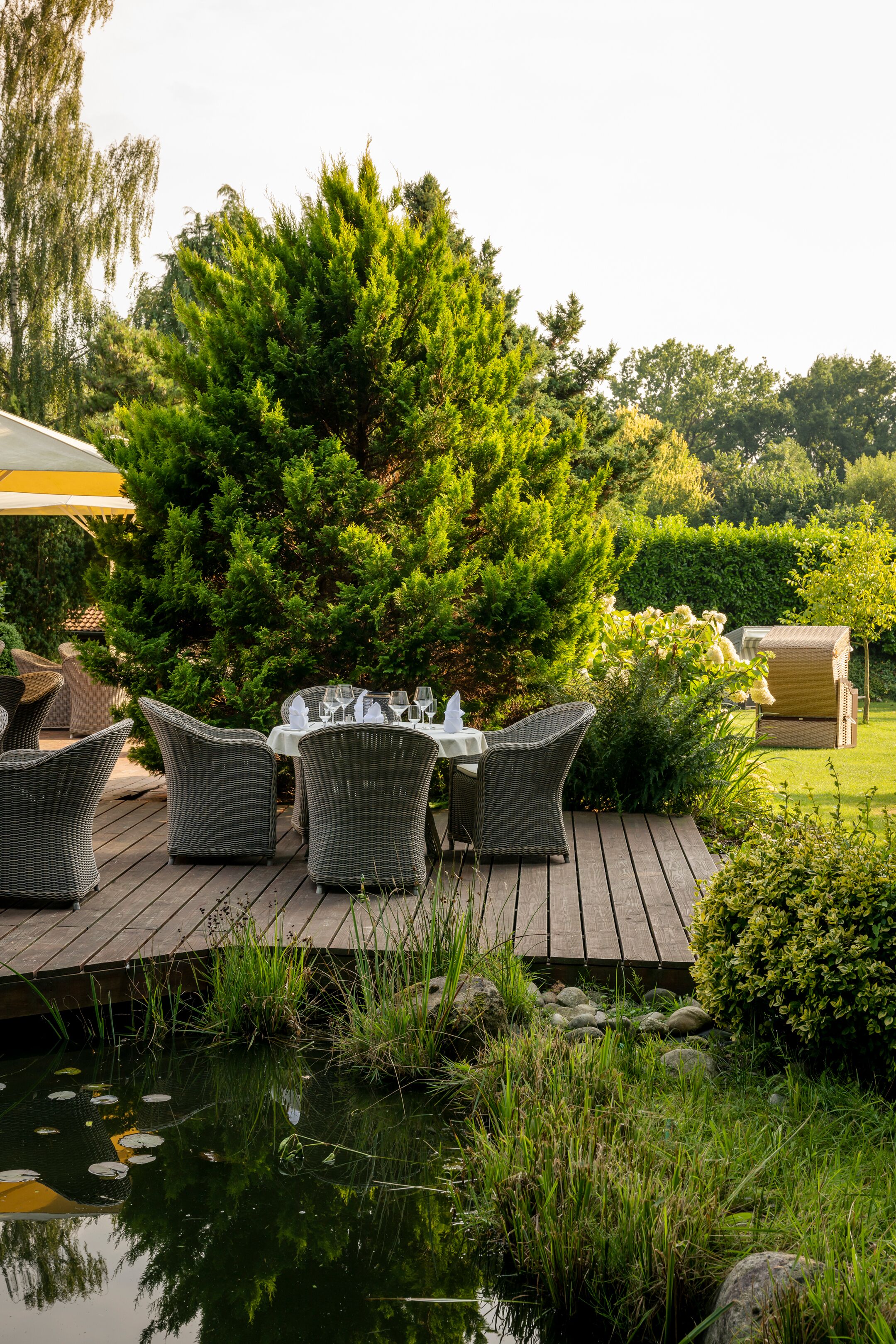 A deck with wicker furniture, a table set for dining, and a pond with lily pads.