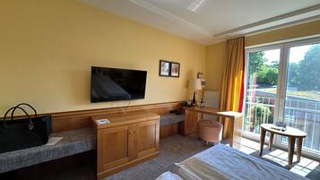 Ein Hotelzimmer mit Bett, Schreibtisch mit Lampe, Fernseher und einem Fenster mit Vorhängen.