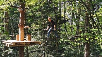 A person navigating a rope course in a forested area with wooden platforms and ropes.