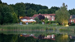 Un hôtel situé au bord d’un lac, dont l’image se reflète dans l’eau, entouré d’arbres et de verdure.
