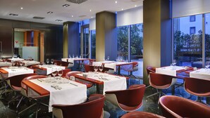 Un restaurant moderne avec des tables dressées pour le service, de grandes fenêtres offrant une vue sur l’extérieur et un décor intérieur contemporain.
