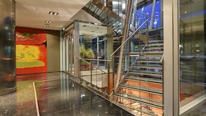 Un intérieur moderne avec un escalier en verre, des revêtements de sol réfléchissants et une fresque murale aux couleurs vives.