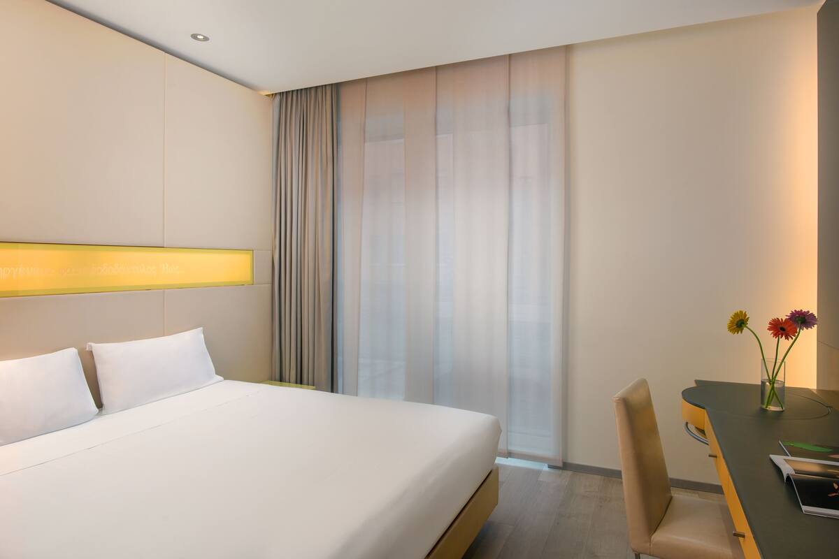 Een hotelkamer met een groot bed, een bureau met stoel en een raam met gordijnen.