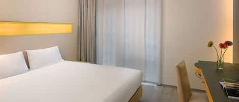 Une chambre d’hôtel avec un grand lit, un bureau avec une chaise et une fenêtre avec des rideaux.