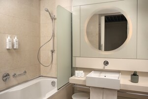 Een moderne badkamer met een bad, een douche met glazen wanden, een ronde spiegel en een wastafel met toiletartikelen.