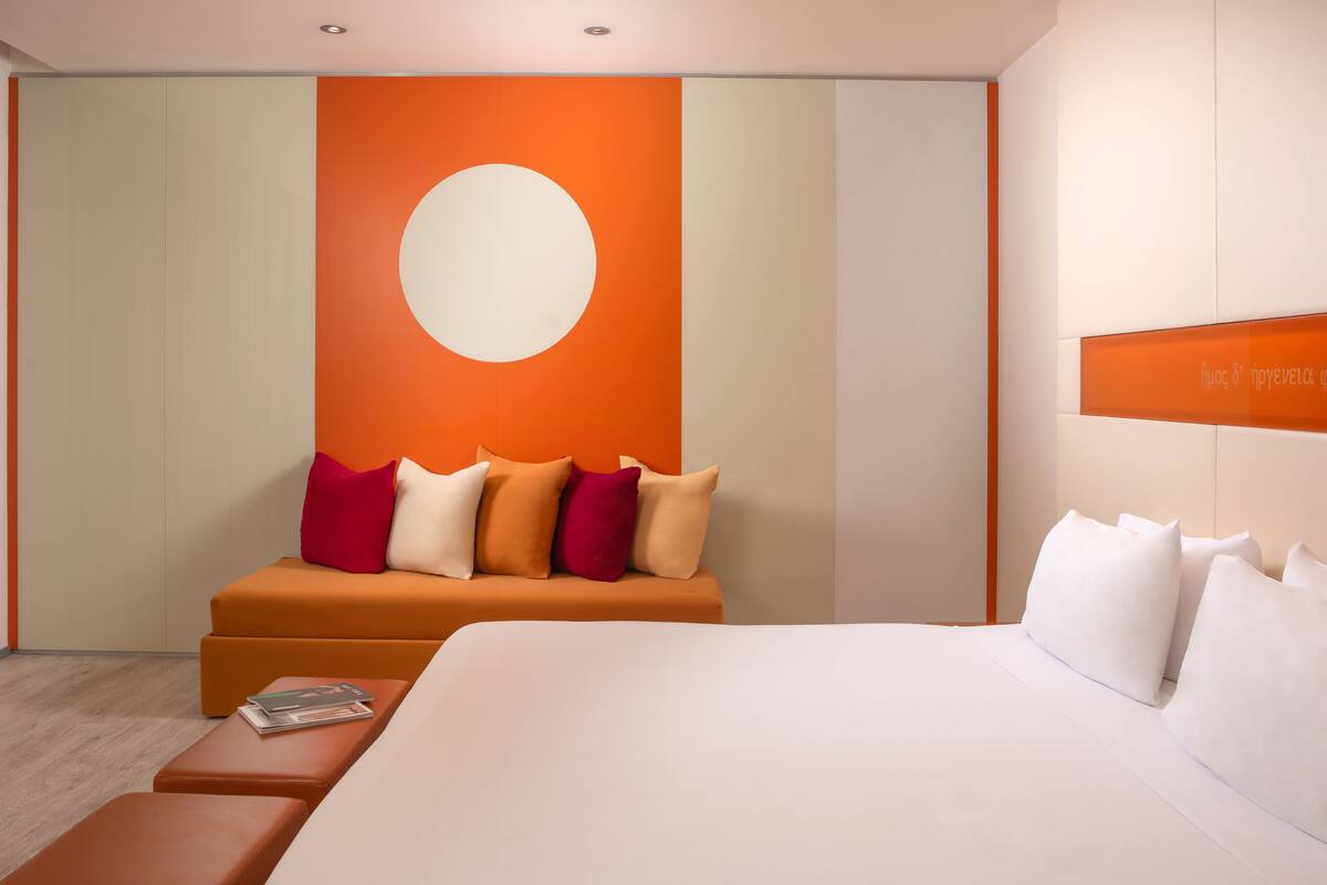 Een moderne hotelkamer met een groot bed, een bank met veel kussens, een bijzettafeltje met een tijdschrift, en een wand met een groot rond ontwerp.