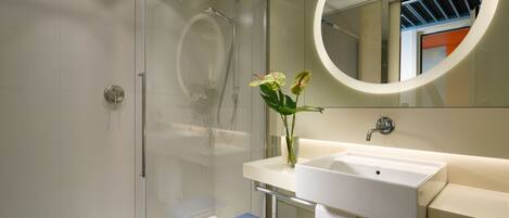 A modern bathroom with a glass shower enclosure, a white sink, and a round mirror.