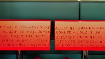 Due sedie rosse con una superficie riflettente, poste di fronte a un muro con del testo.